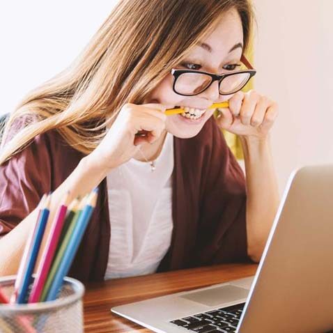 woman biting a pencil in frustration while looking at computer screen